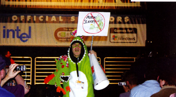Tristan in a green murloc costume holding a protest sign and megaphone on the convention floor